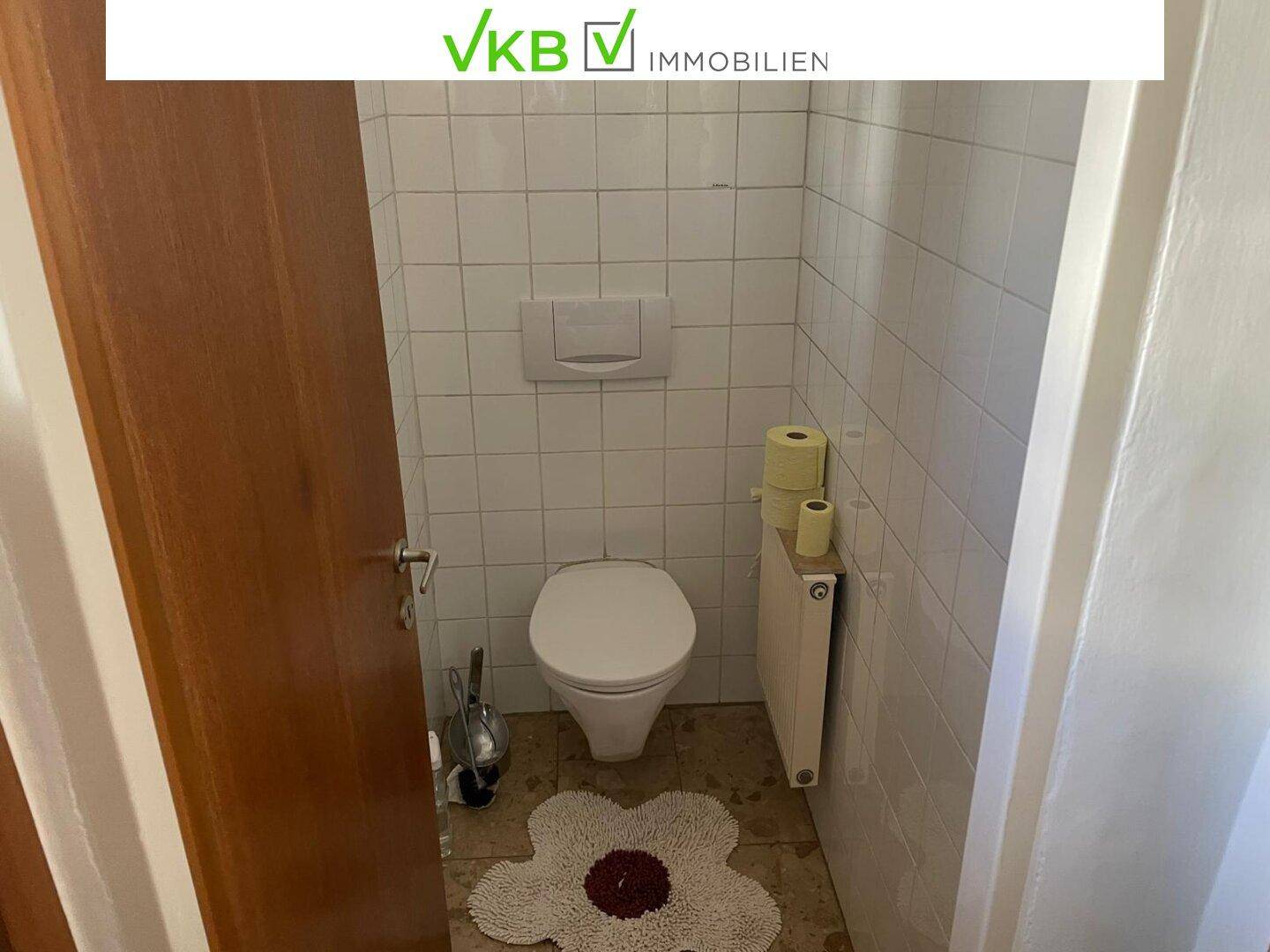 Kleines Gäste-WC mit Toilette, Heizkörper und weißen Wandfliesen.