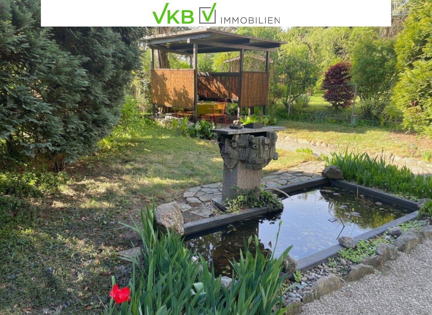 Idyllischer Gartenteich mit Wasserspiel und üppiger Bepflanzung im Vordergrund.