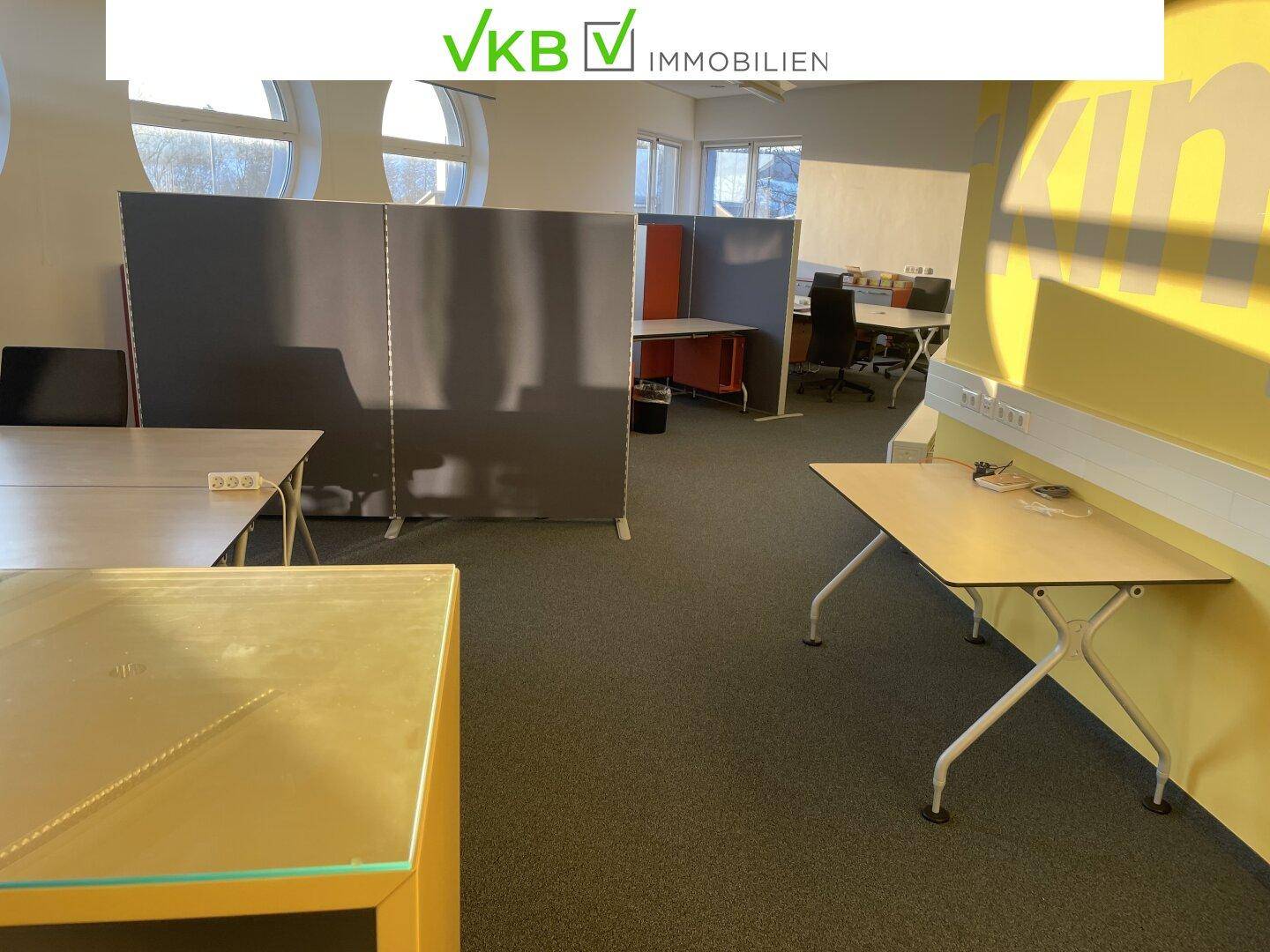 Offener Co-Working-Bürobereich mit Schreibtischen, Raumteilern und großen Fenstern für viel Tageslicht.