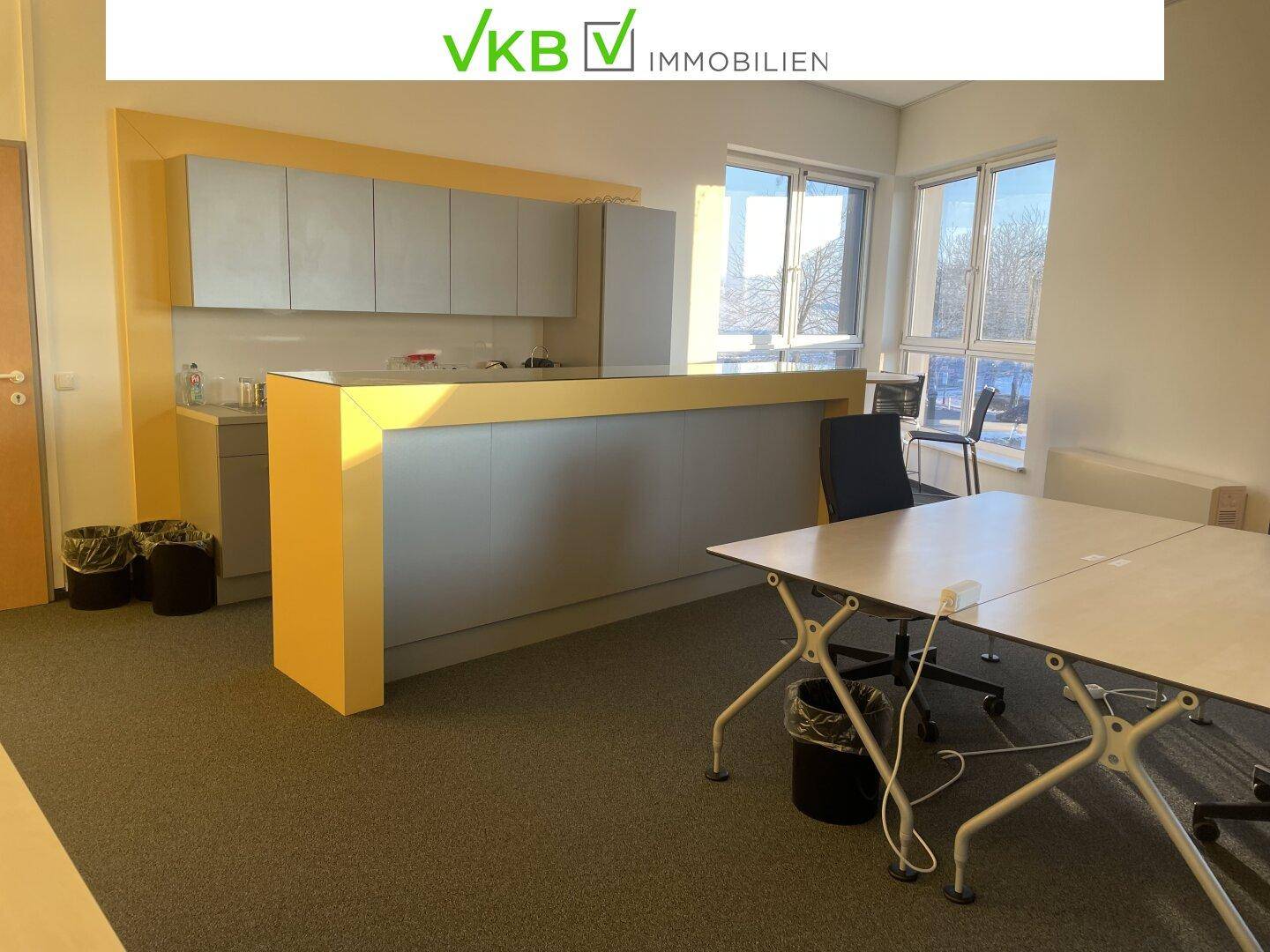 Büro-Küchenzeile mit Theke, Arbeitsbereich und Tischen, ideal für Pausen und informelle Treffen.