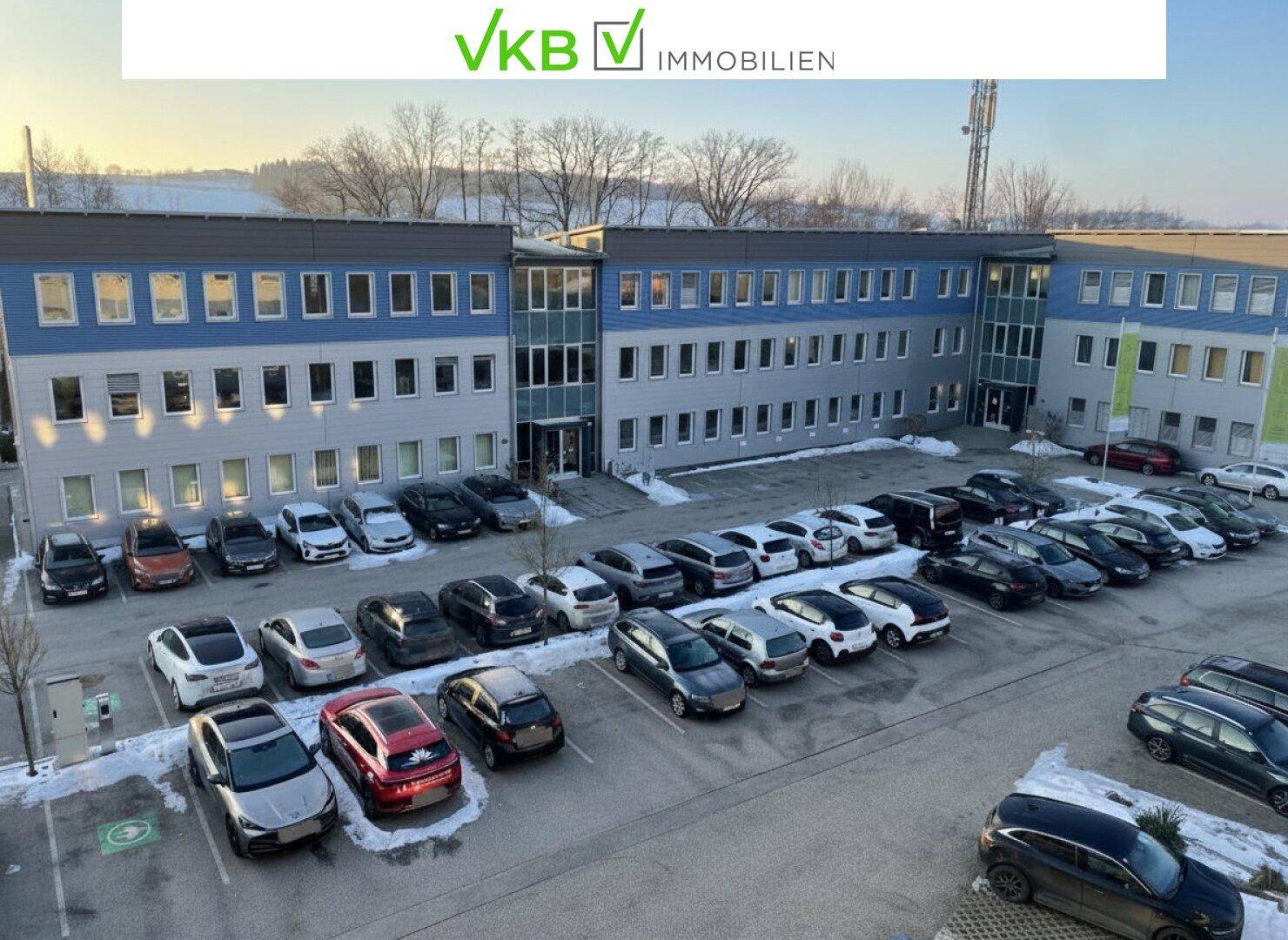 Bürogebäude mit großem Parkplatz und umliegender Winterlandschaft, von oben fotografiert.