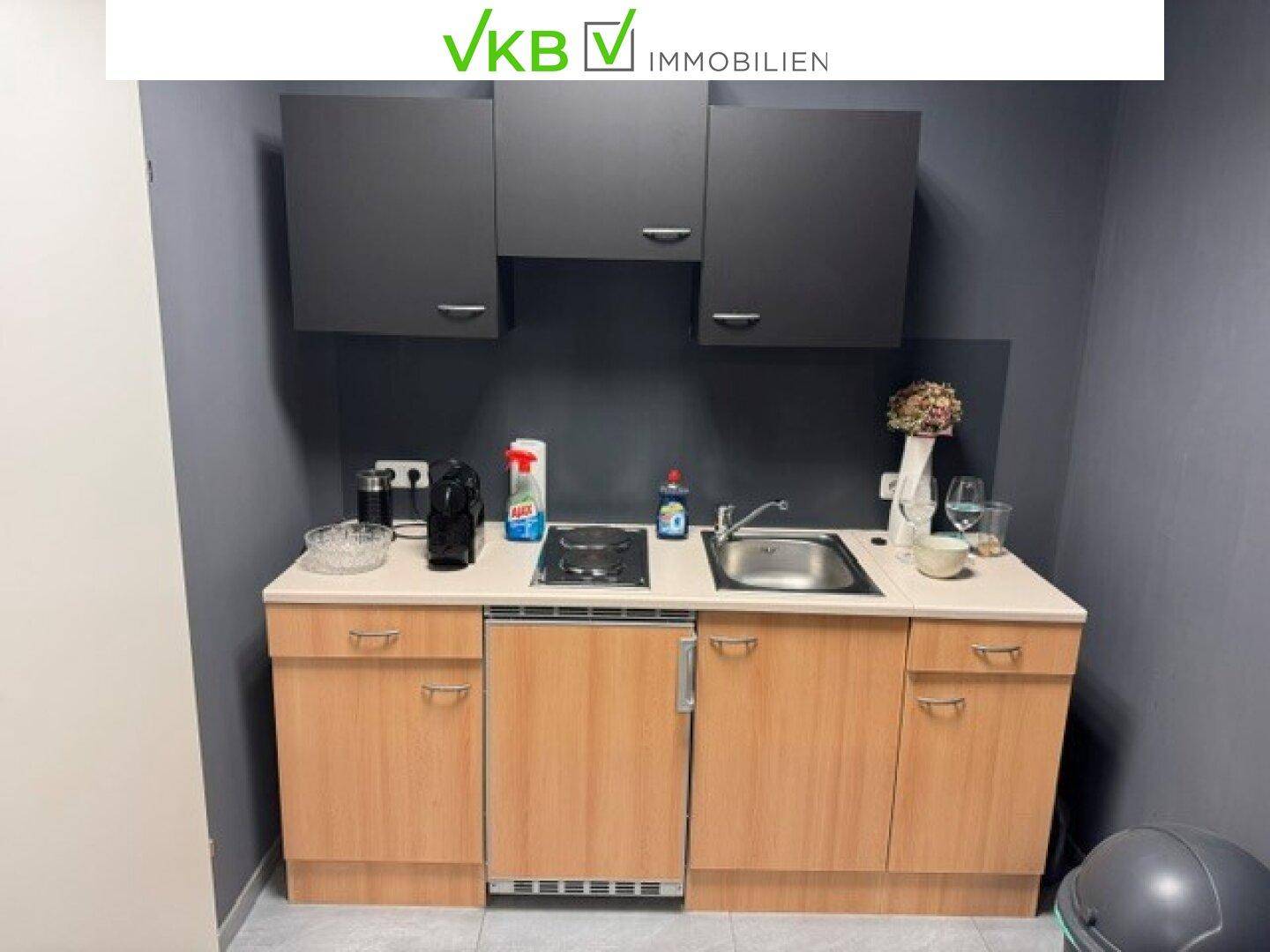 Funktionale Küchenzeile mit Holzschränken, Spüle, Kochfeld und Kühlschrank in einem kompakten Design.