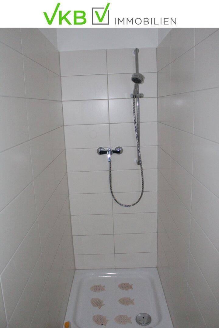 Einfache Duschkabine mit weißen Fliesen und einer Handbrause, funktional und sauber.