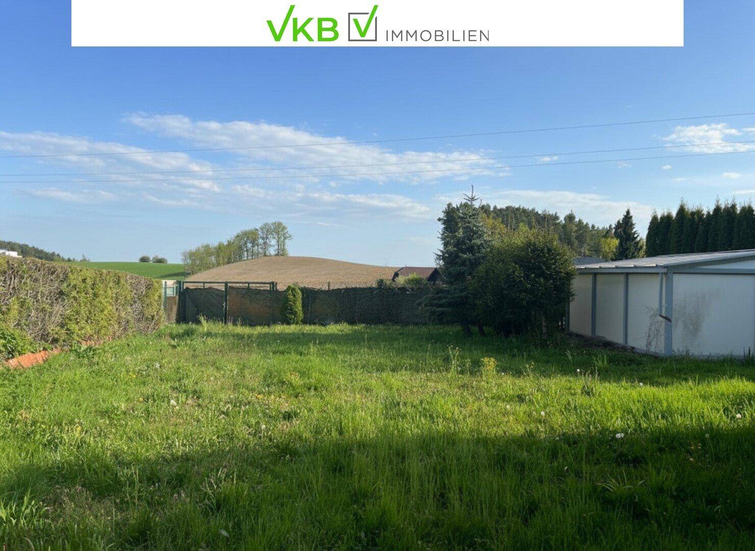 Großes Grundstück mit Rasenfläche, umgeben von Hecken und Blick auf die umliegende Landschaft.