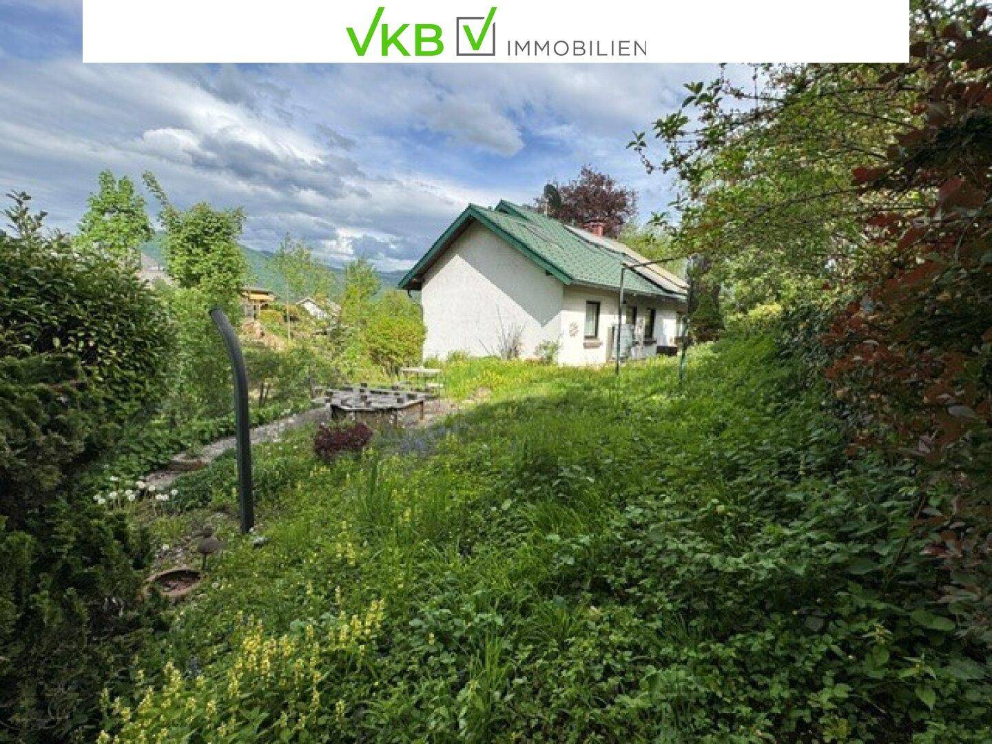 Einfamilienhaus mit grünem Dach, umgeben von üppiger Vegetation und einem Garten.