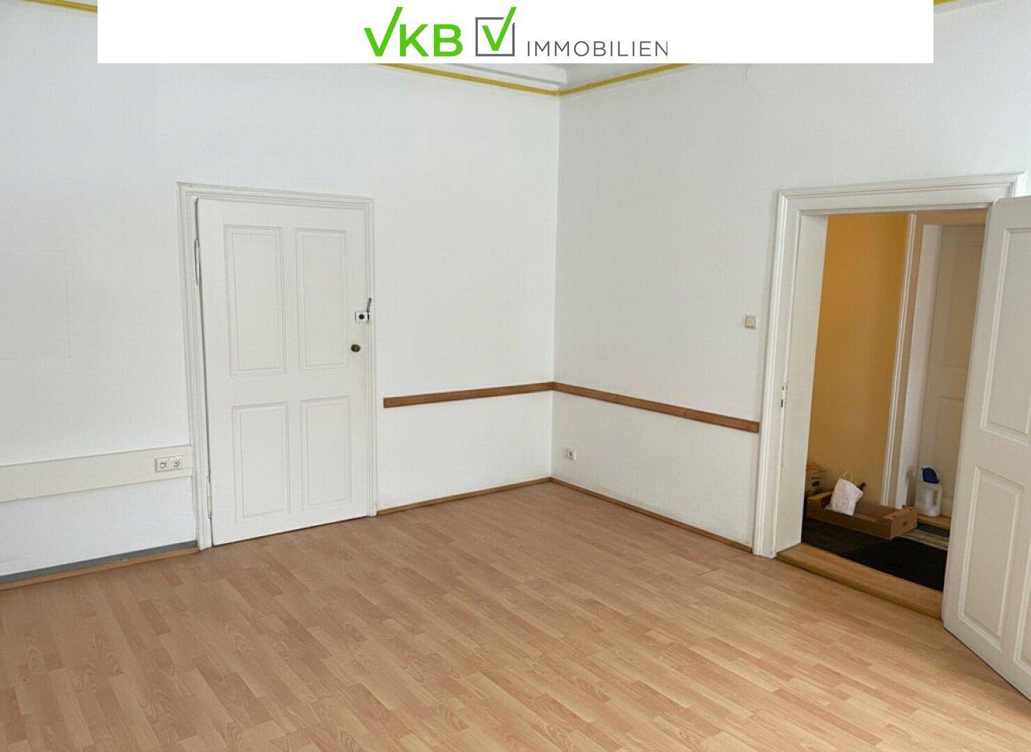 Leerer Raum mit hellem Laminatboden, weißen Wänden und zwei Türen, bereit zur Gestaltung.