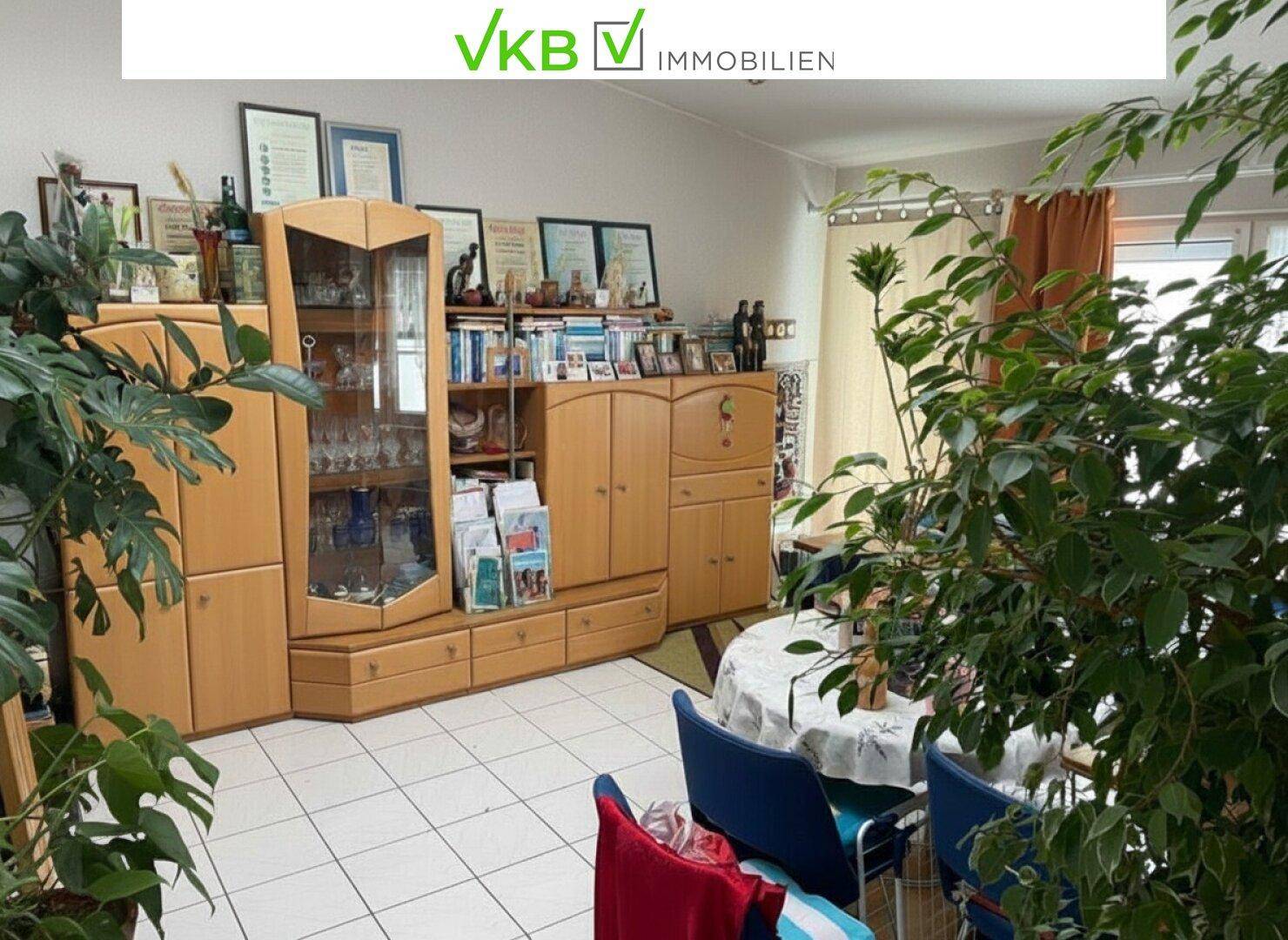Wohn-Essbereich mit weißen Fliesen, Holzmöbeln und vielen Pflanzen, gemütlich eingerichtet.
