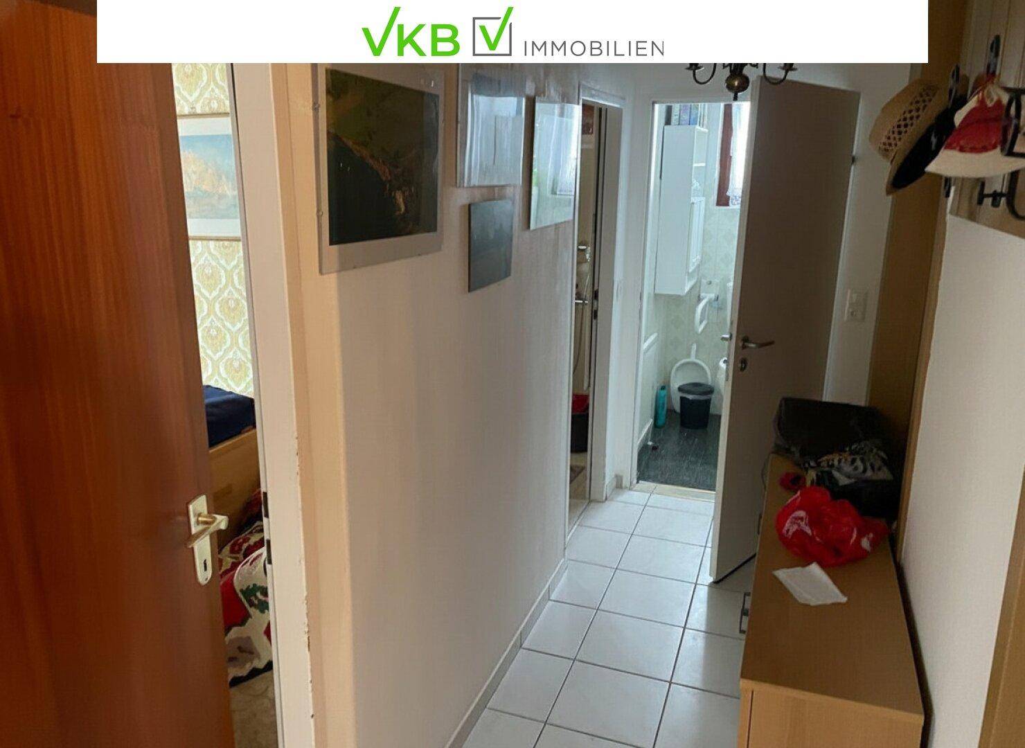 Schmaler Flur mit weißen Fliesen und Blick in ein Badezimmer am Ende.