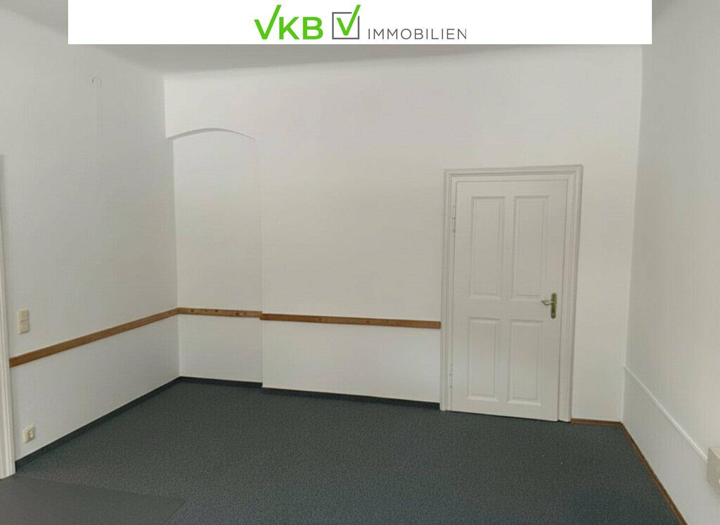 Leerer Raum mit dunklem Teppichboden, weißen Wänden und einer weißen Tür.