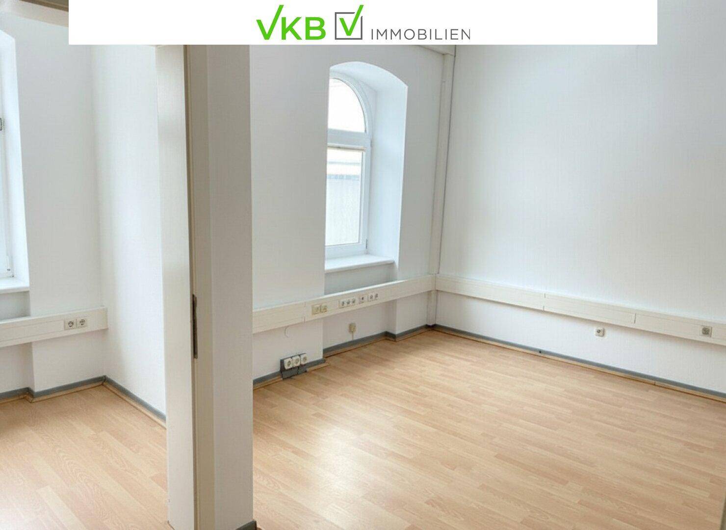 Heller Raum mit Laminatboden, weißen Wänden und zwei Fenstern, eines davon gewölbt.