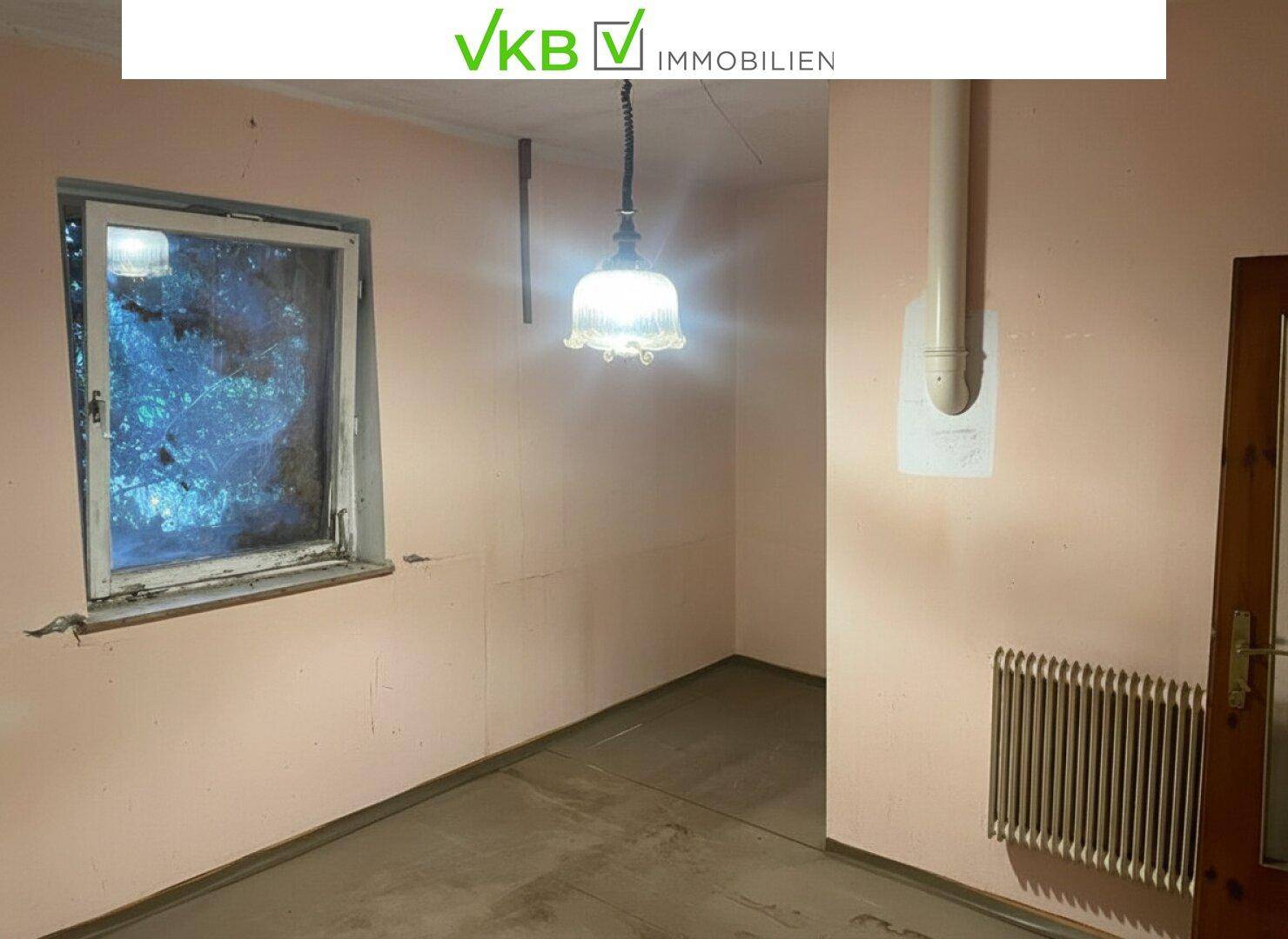 Leerer Raum mit rosa Wänden, einem Fenster und Heizkörper, bereit zur Renovierung.