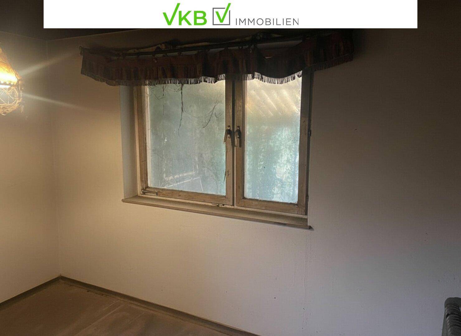 Unmöblierter Raum mit großem Fenster und einfacher Fensterdekoration, sanierungsbedürftig.