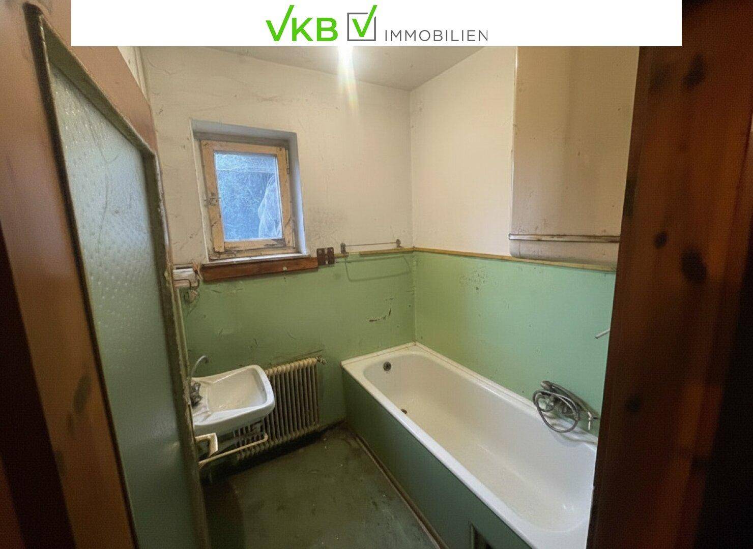Badezimmer im Stil der 80er Jahre mit Badewanne, kleinem Waschbecken und grünen Wänden.