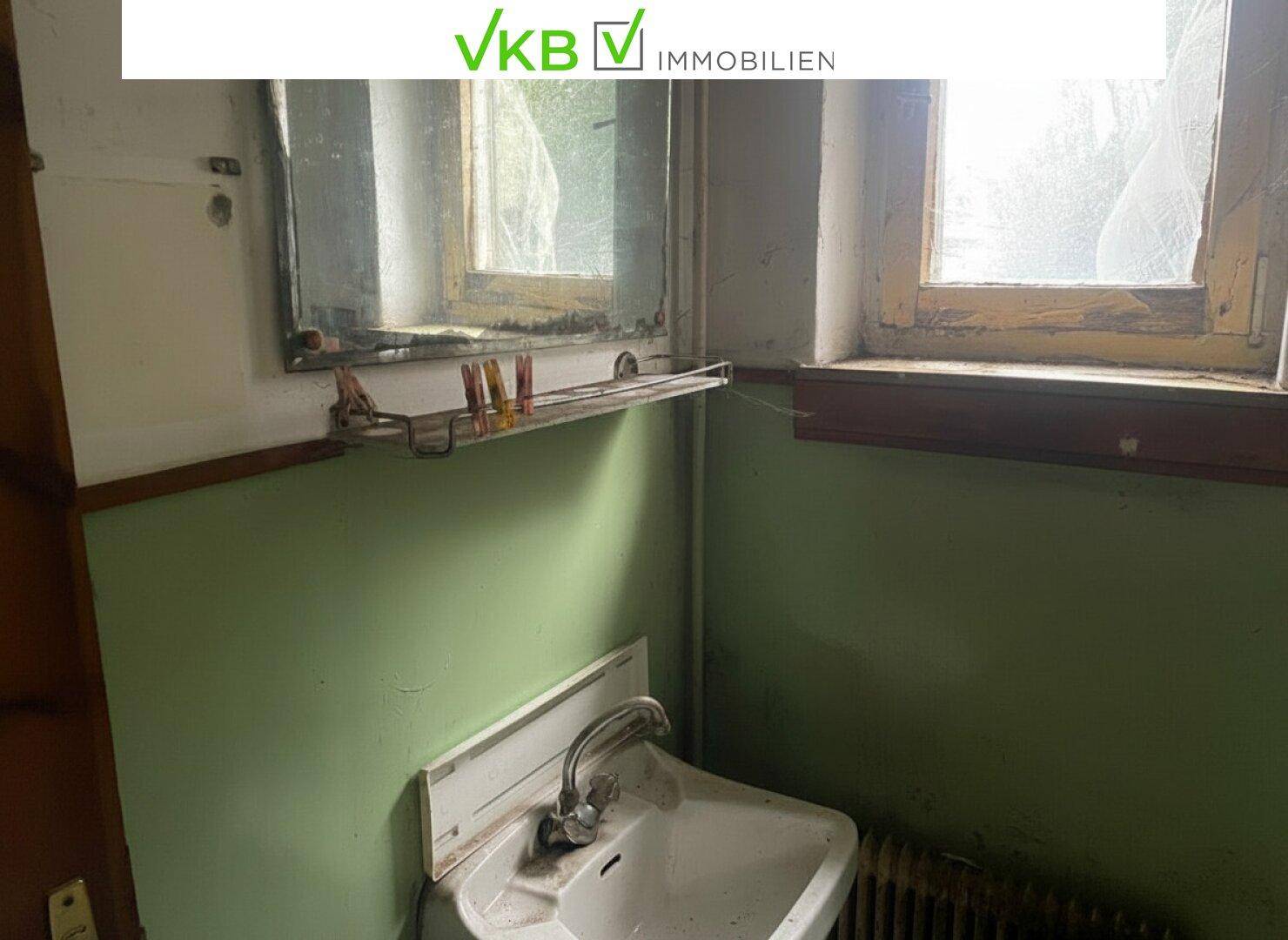 Detailansicht des Waschbeckens und Spiegels in einem Badezimmer mit grünen Fliesen.