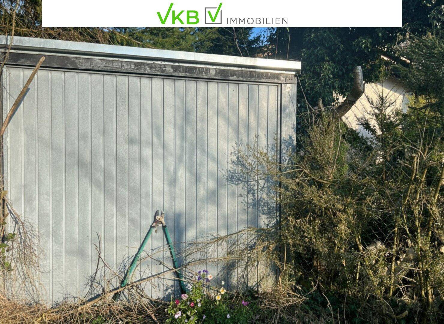 Metallgarage umgeben von dichtem Bewuchs und Sträuchern im Außenbereich.