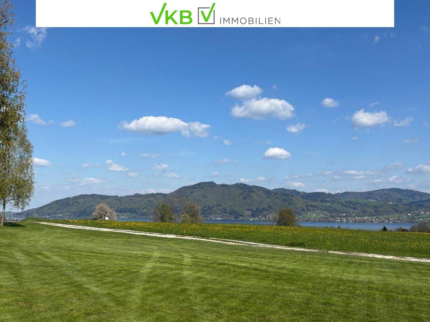 Idyllische Landschaft mit weitem Grünflächen, einem See und sanften Hügeln am Horizont.