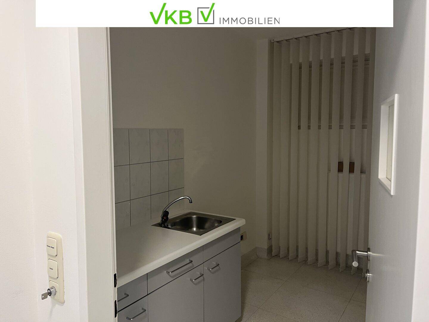 Kleine Küchenzeile mit Spülbecken, Unterschränken und Fliesenrückwand in einem hellen Raum.