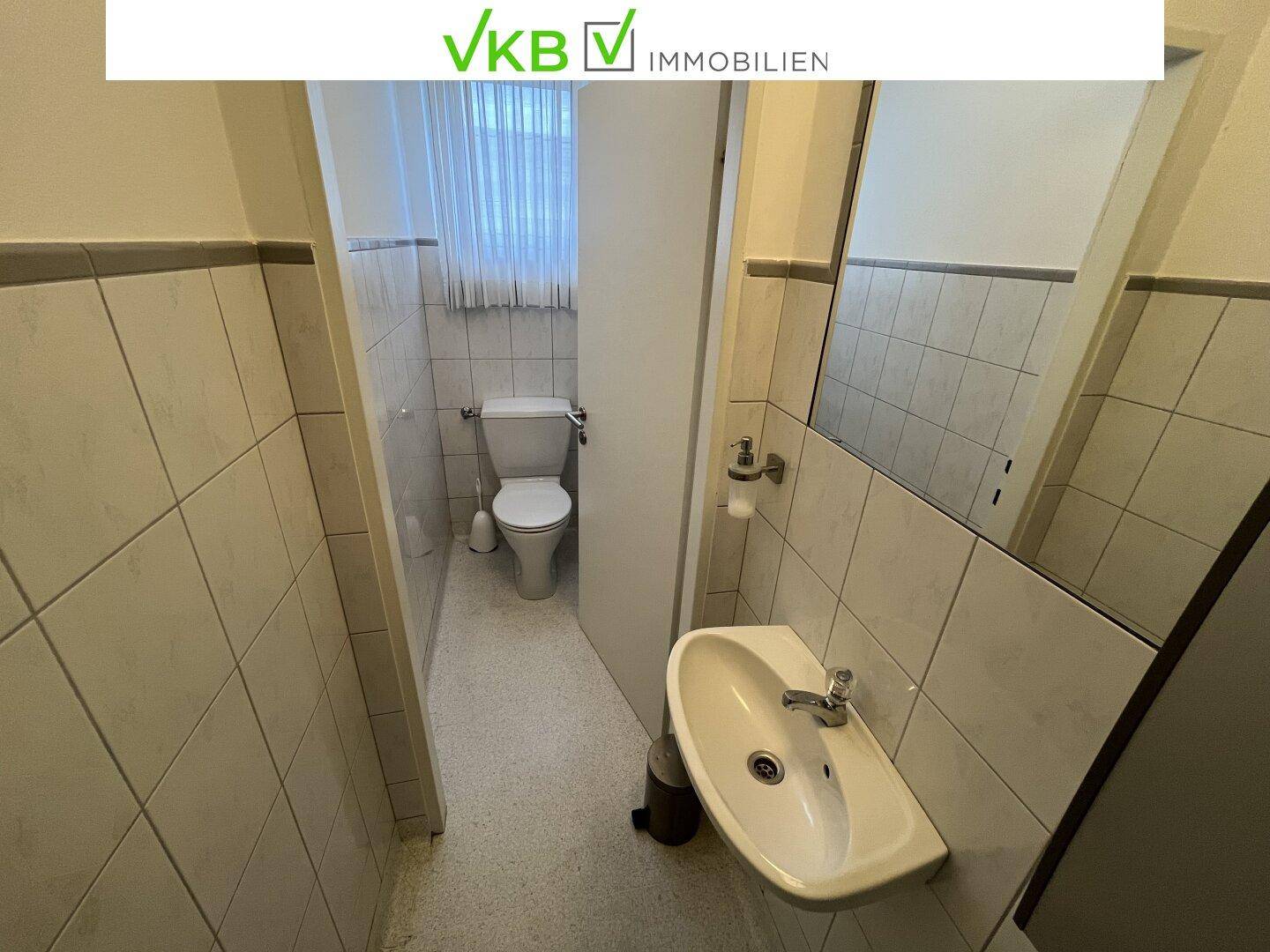 Kleines Badezimmer mit WC, Waschbecken und Spiegel, komplett gefliest in hellem Design.