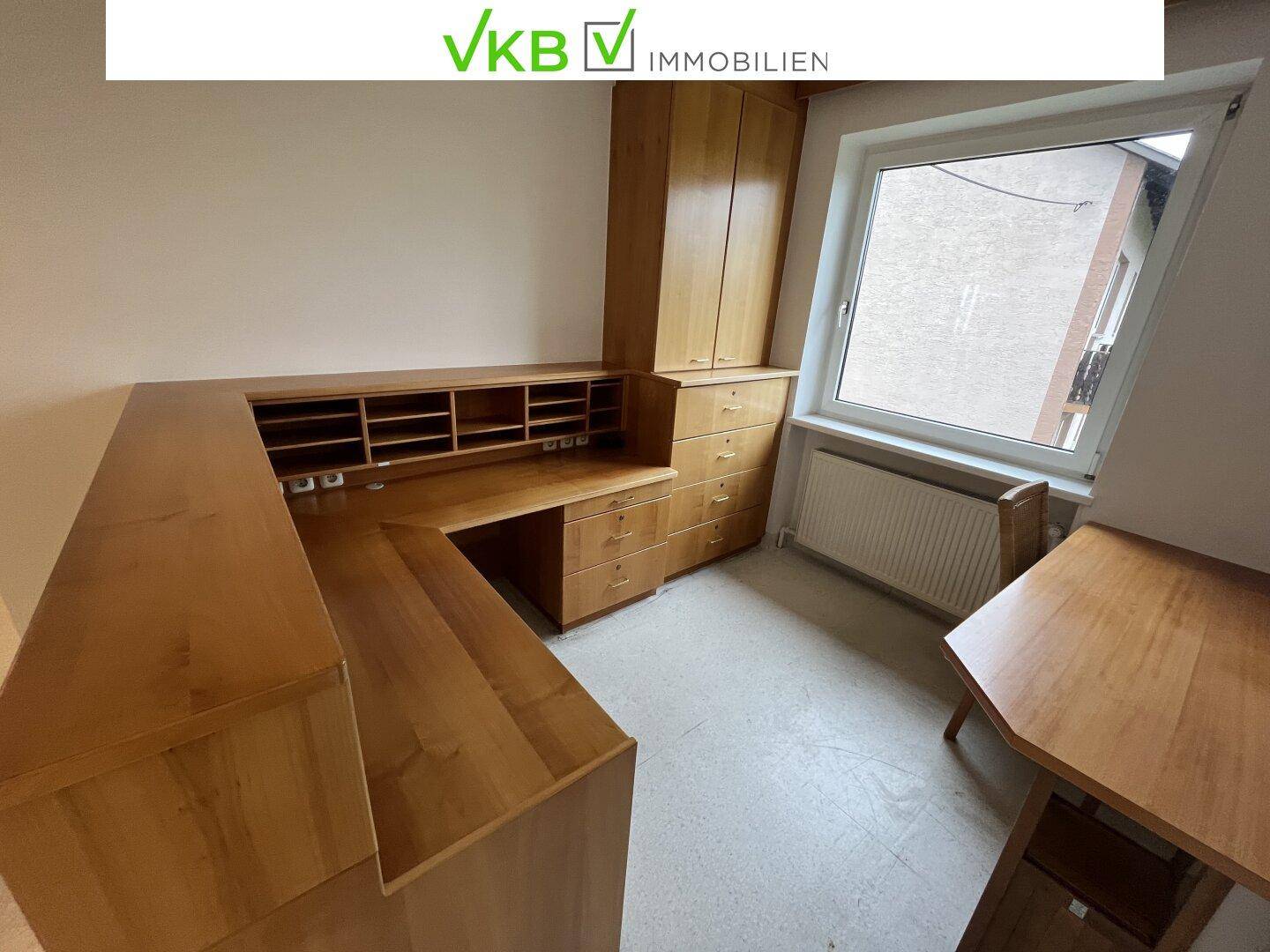 Geräumiger Büroraum mit einem großen Holzschreibtisch und Schränken, gut beleuchtet durch ein Fenster.