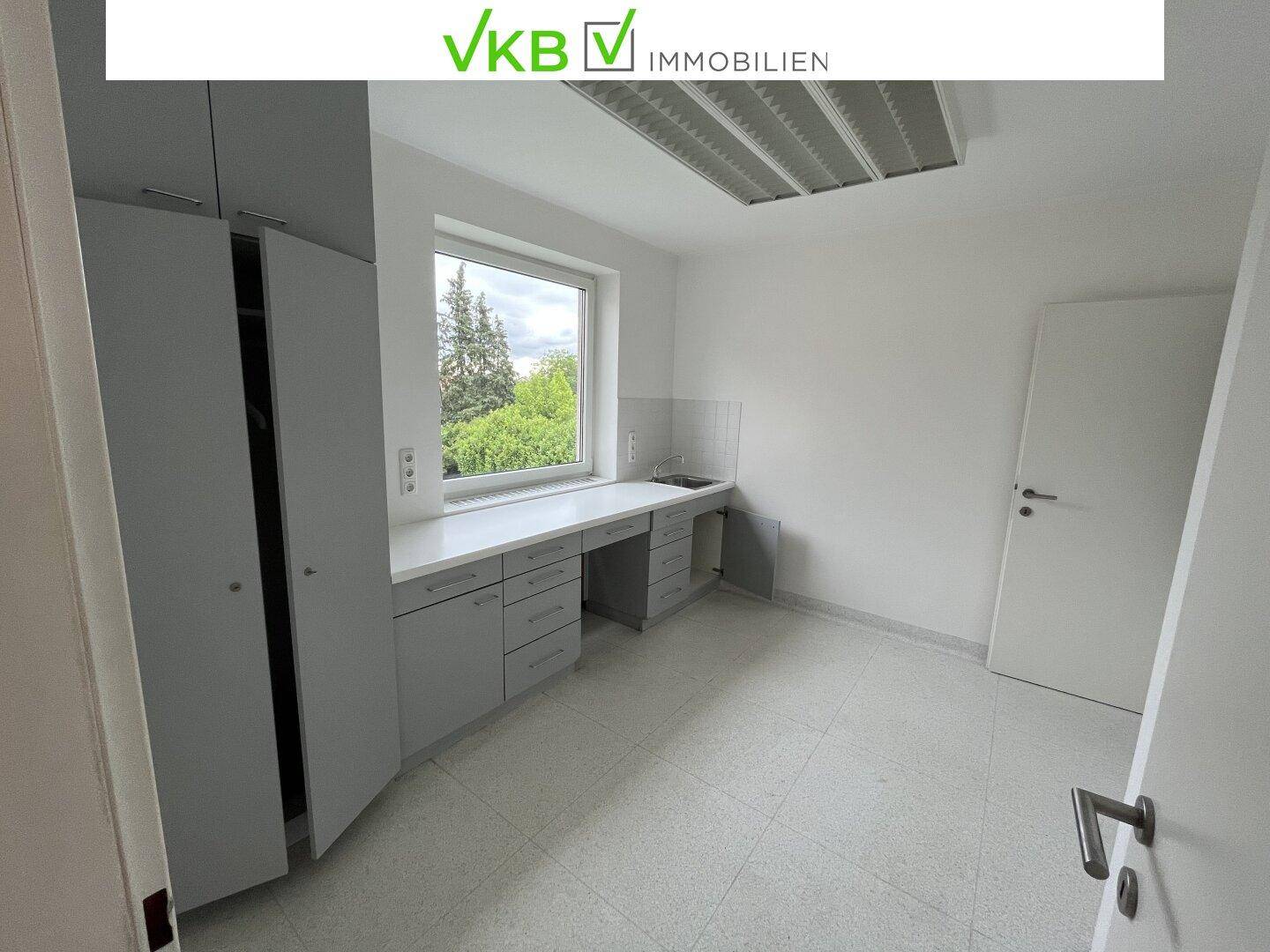 Heller Büroraum mit Einbauschränken, Arbeitsplatte und Fenster mit Blick ins Grüne.