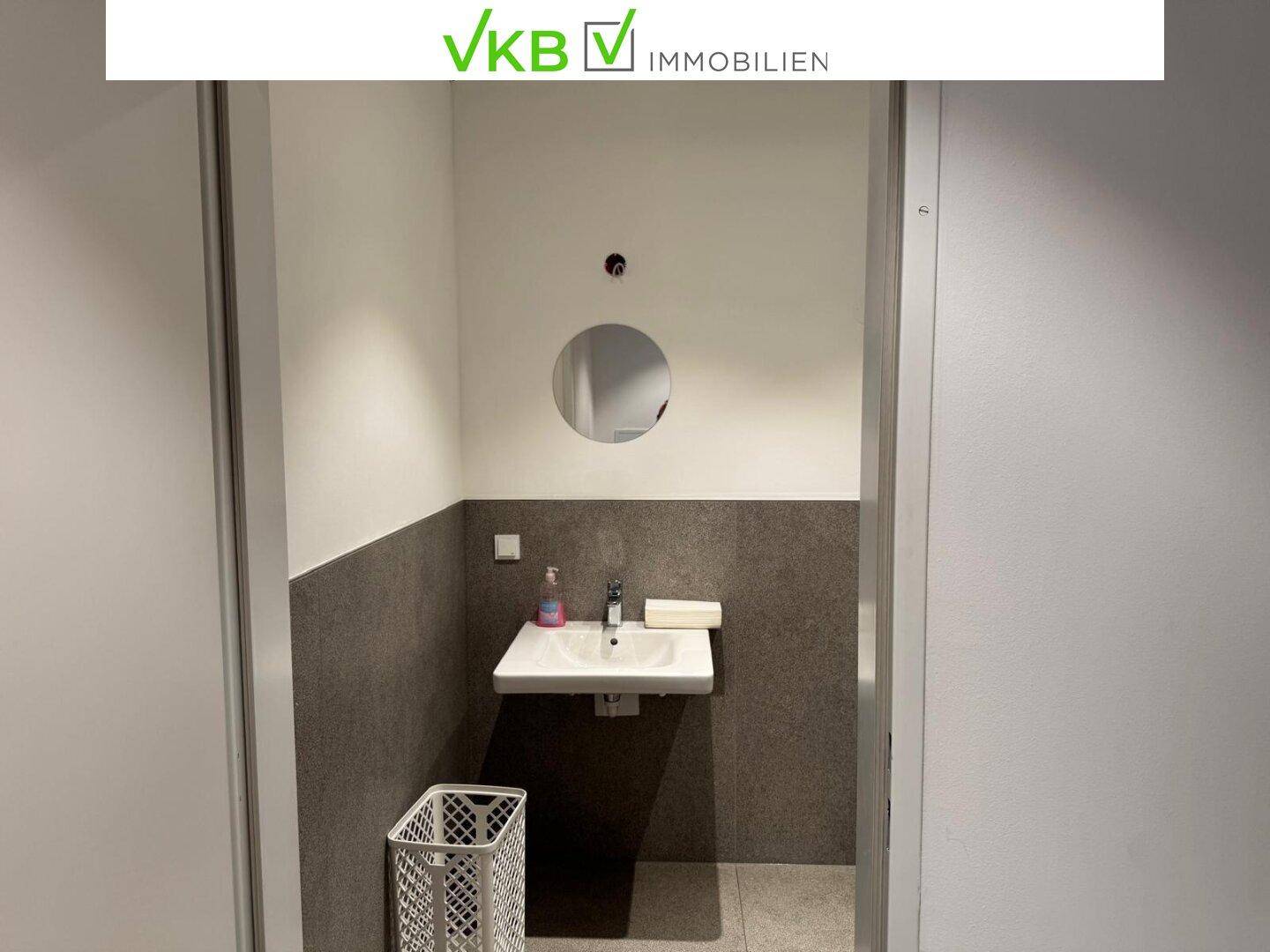 Eingangsbereich eines Gäste-WCs mit Waschbecken und rundem Spiegel, schlicht und funktional.