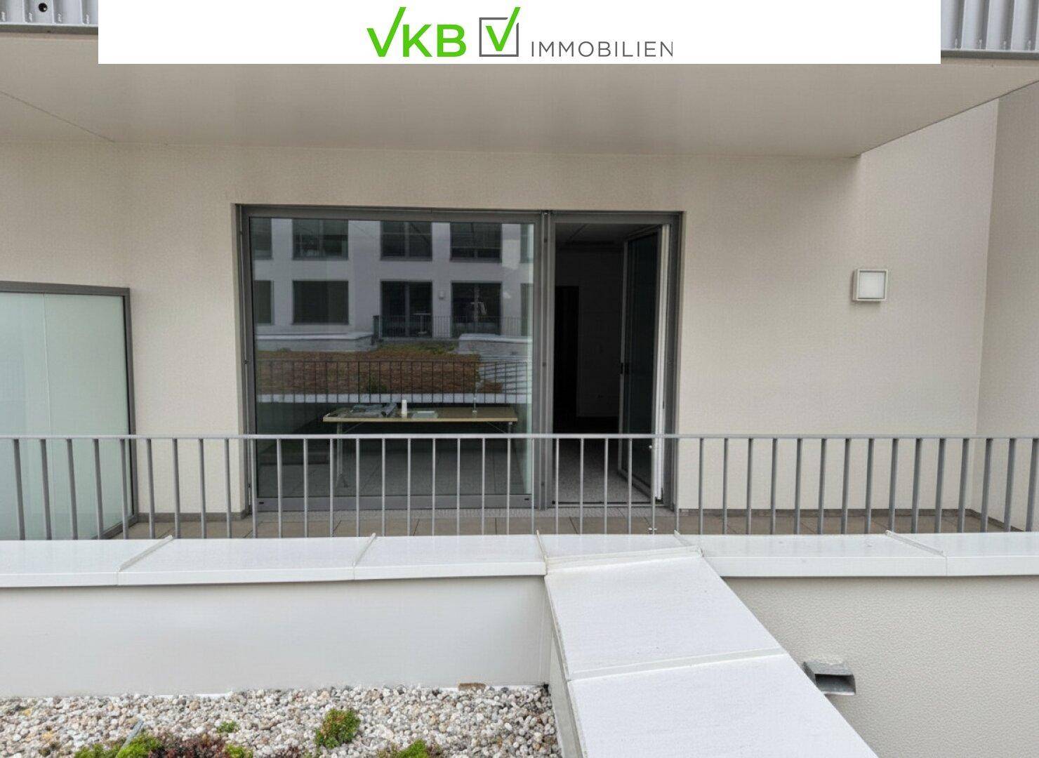Geräumige Terrasse mit Metallgeländer und Zugang zum Innenbereich, bietet einen Blick auf umliegende Gebäude.