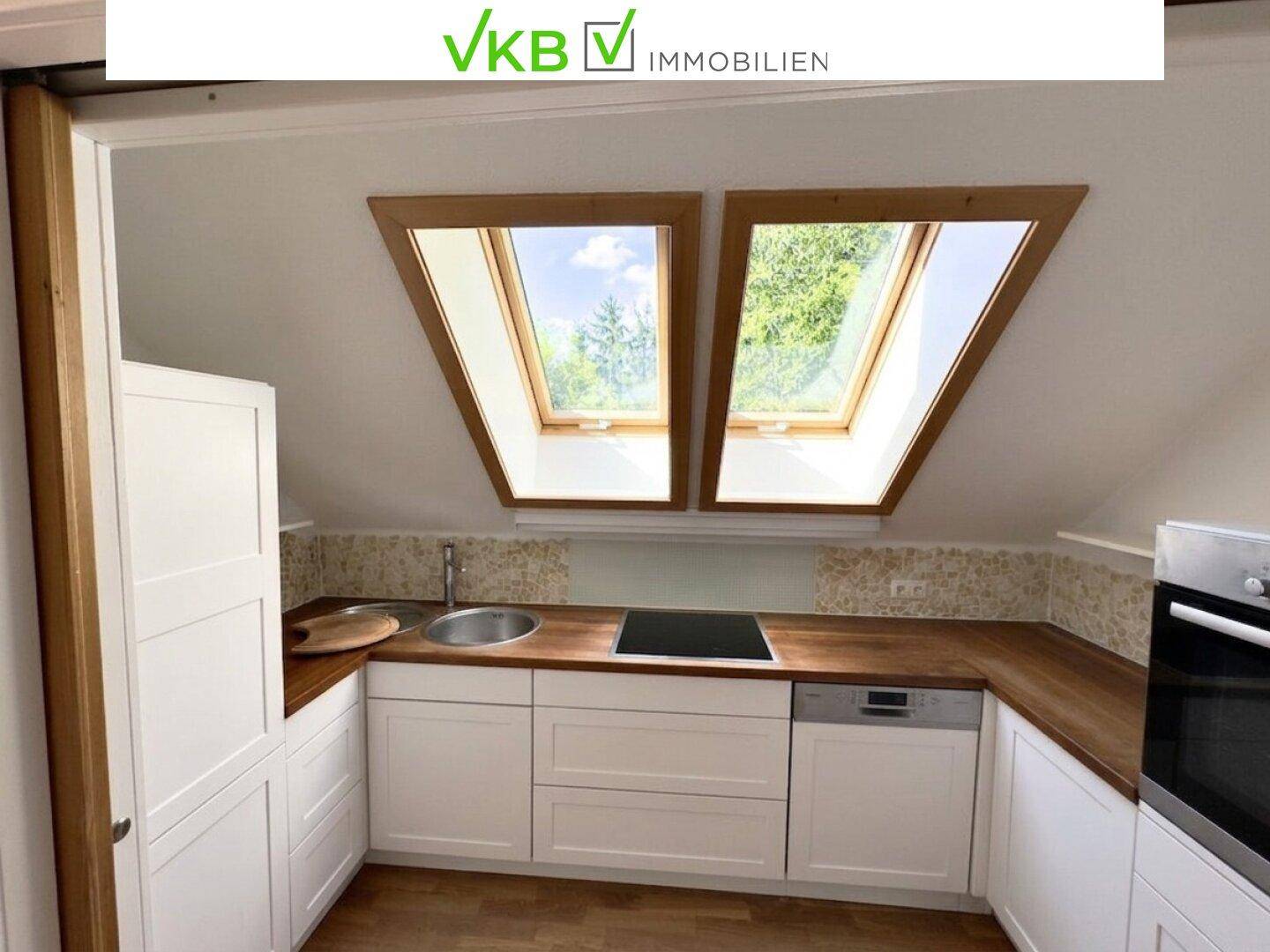 Moderne Küche im Dachgeschoss mit weißen Schränken, Holz-Arbeitsplatte und Dachfenstern.