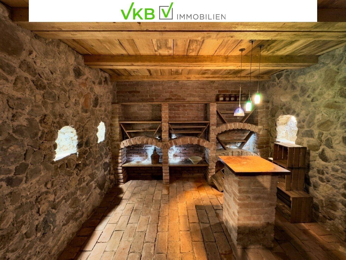 Historischer Weinkeller mit Ziegel- und Steinwänden, Holzbalkendecke und Weinregalen.