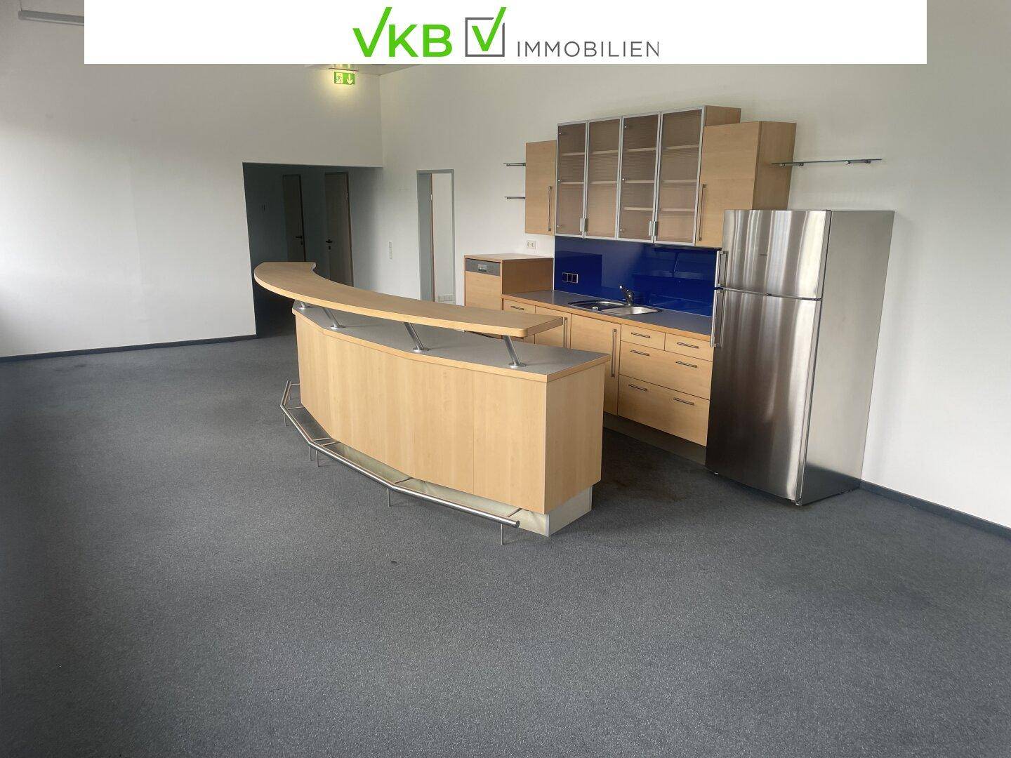 Geräumige Teeküche mit Bartheke, Holzschränken und einem Kühlschrank in einem offenen Bereich.