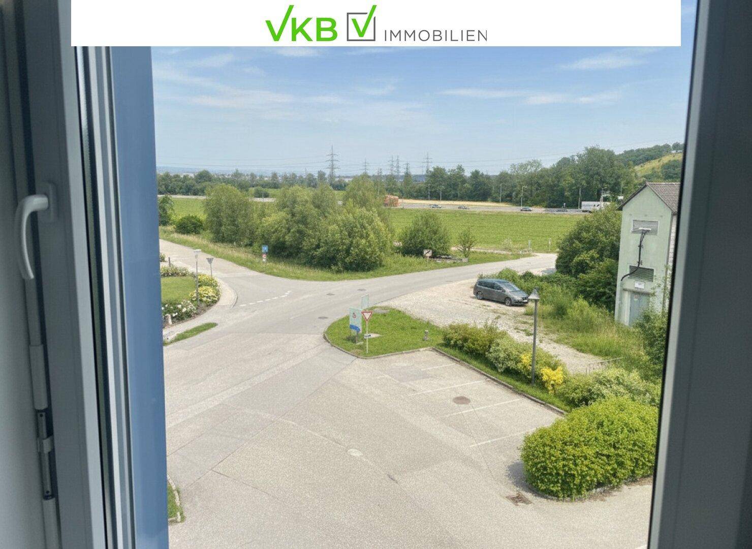Ausblick aus einem Fenster auf eine ländliche Umgebung mit Straßen, Bäumen und Hügeln.