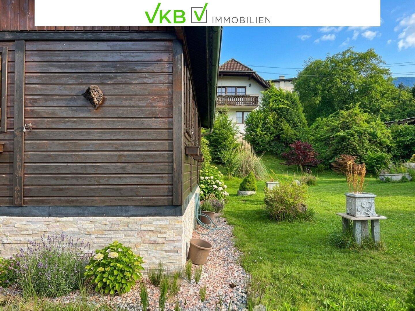 Seitenansicht des Holzhauses mit Holzfassade und einem gepflegten Gartenbereich mit Kies und Pflanzen.