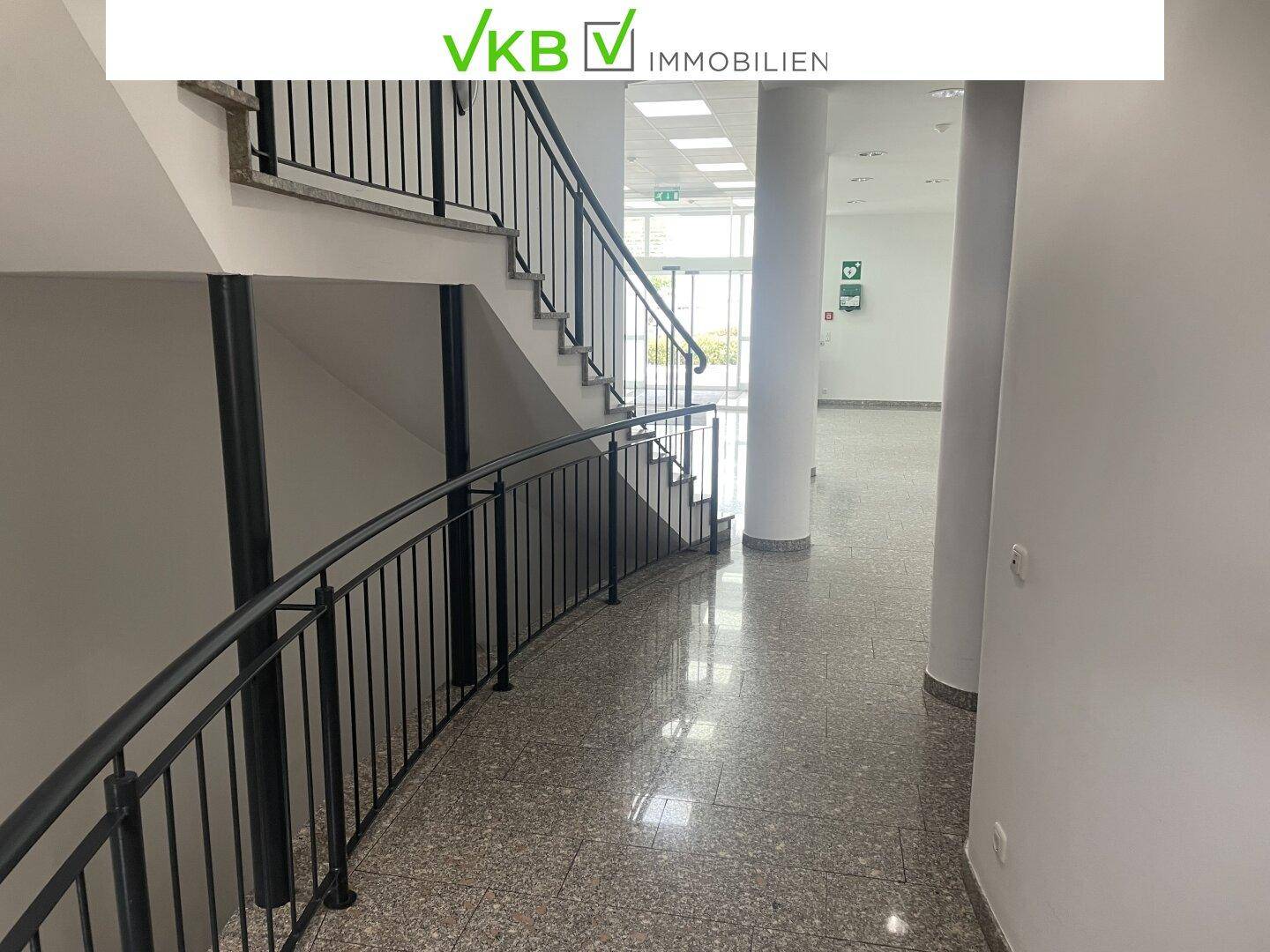 Heller Treppenaufgang mit Granitboden und schwarzem Metallgeländer in einem Bürogebäude.