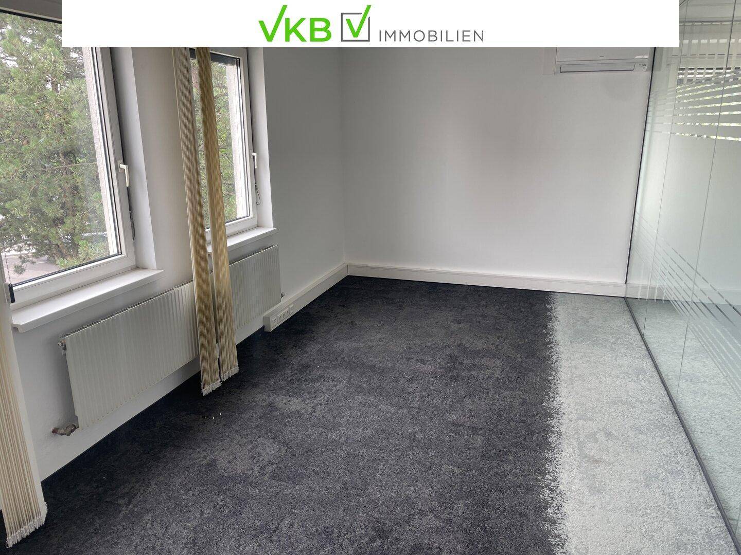 Helles Einzelbüro mit Teppichboden und großen Fenstern, die viel Tageslicht hereinlassen.