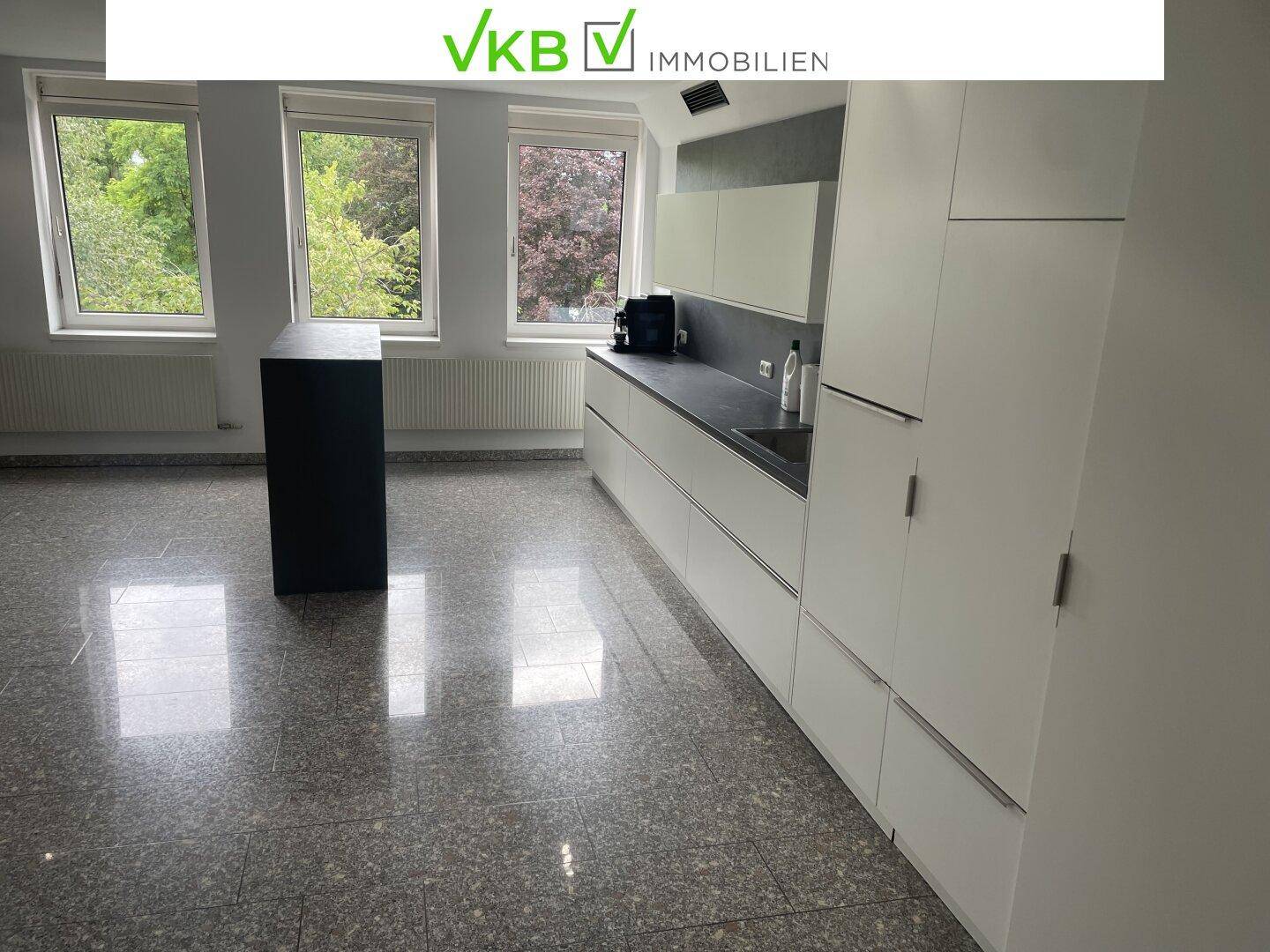Funktionale Teeküche in einem Büroraum mit modernen weißen Schränken und Granitboden.