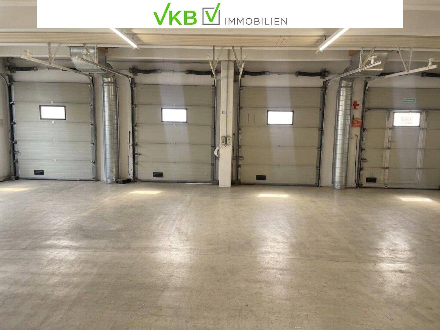 Großer Lagerraum mit vier Rolltoren und robustem Betonboden, ideal für Logistik.