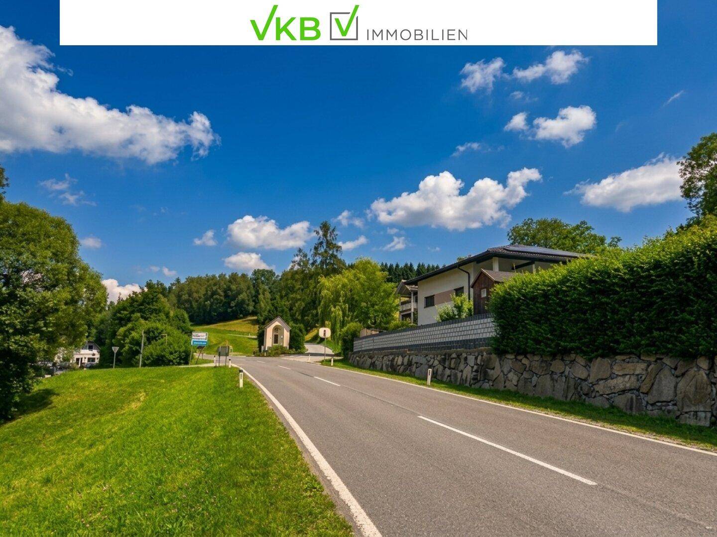 Ländliche Straße mit einem Wohnhaus und grüner Landschaft unter strahlend blauem Himmel.