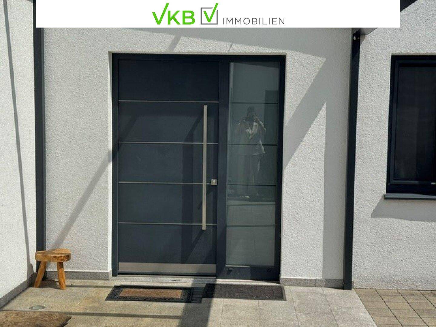 Moderner Eingangsbereich mit dunkler Haustür, Glasseitenteil und weißer Fassade eines Neubaus.