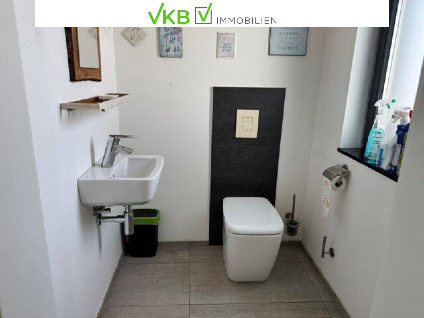 Praktisches Gäste-WC mit wandhängender Toilette, kleinem Waschbecken und Fenster.