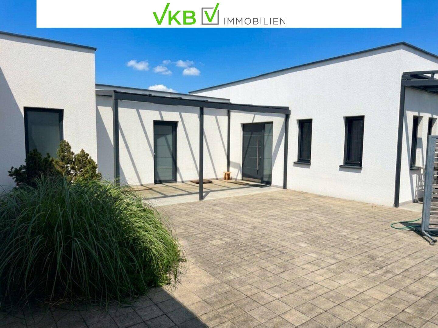 Moderne Hausfassade mit gepflastertem Vorplatz und überdachtem Eingangsbereich.