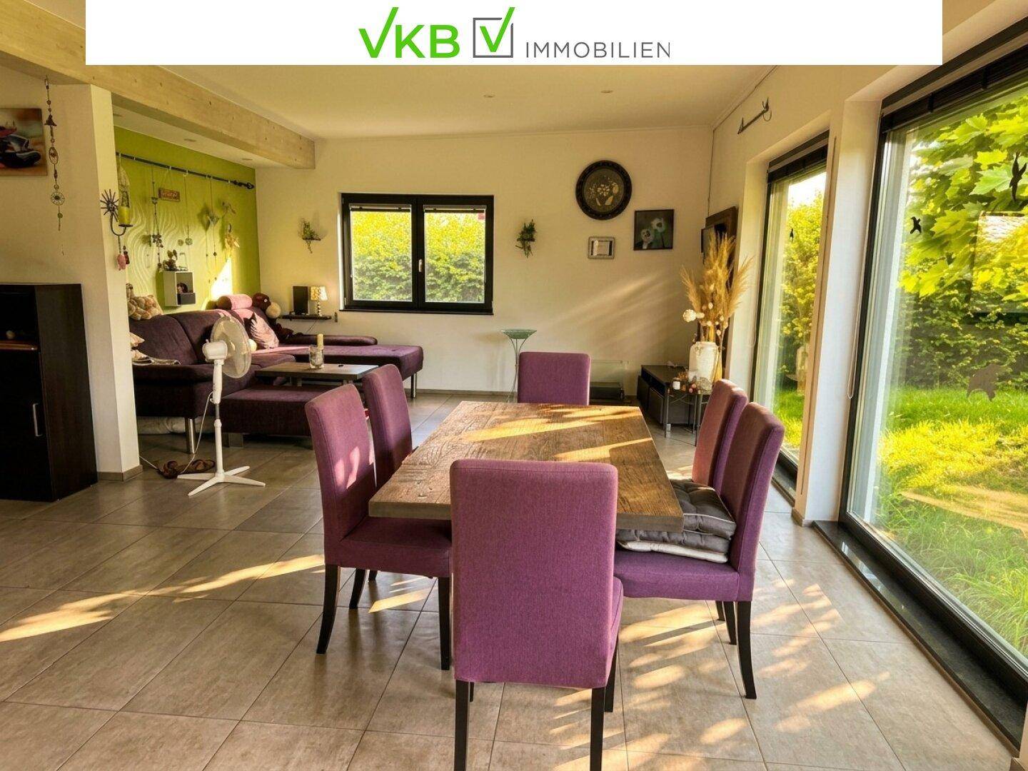 Heller Wohn-Essbereich mit großem Holztisch, lila Stühlen und Blick in den Garten.