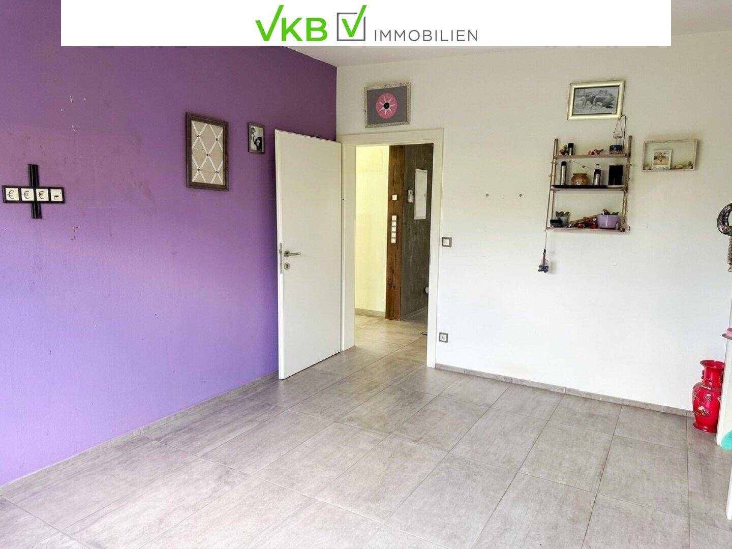 Helles Zimmer mit Fliesenboden und lila Wänden, bietet Zugang zu weiteren Räumen.