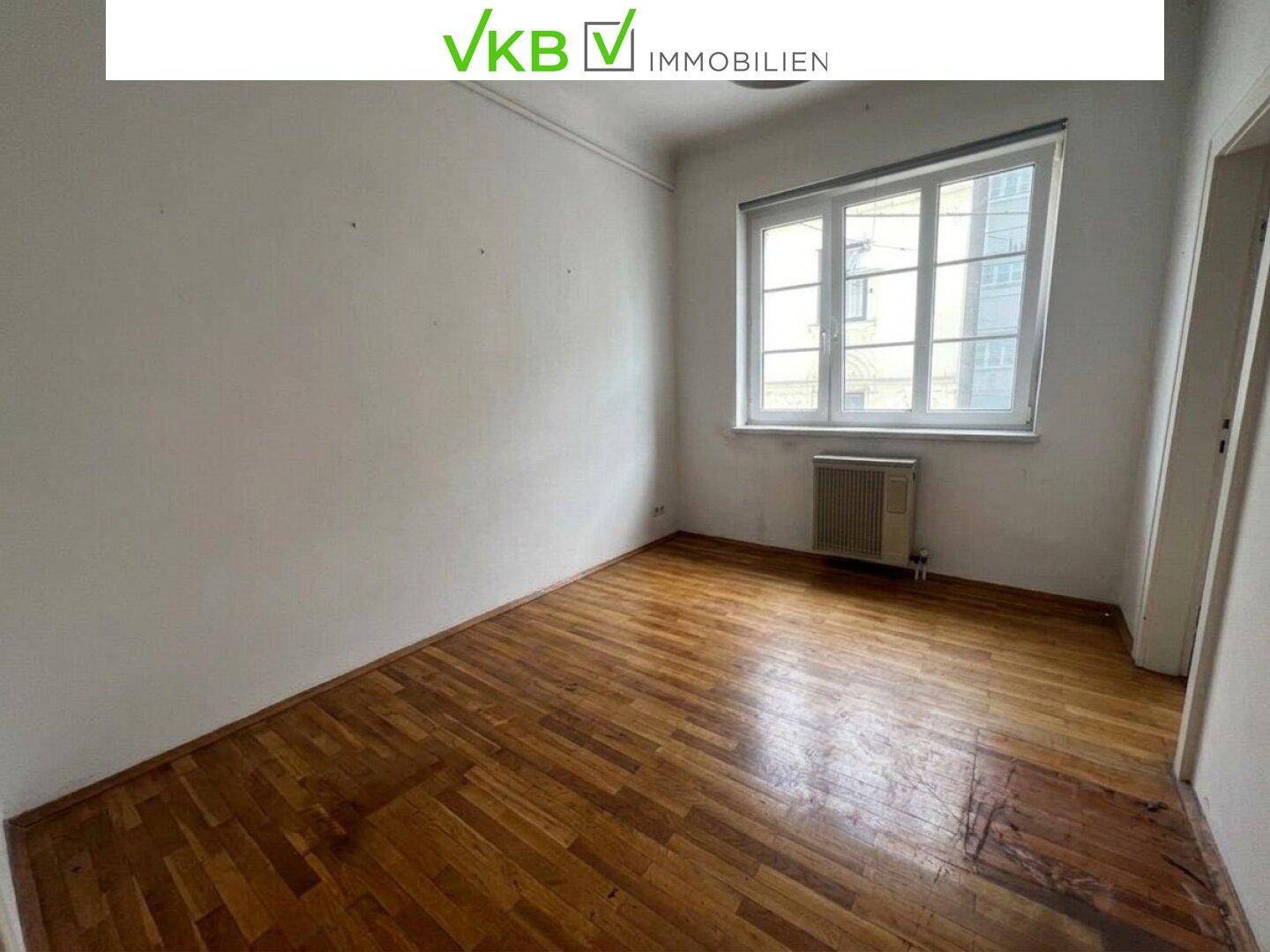 Leeres Schlafzimmer mit Holzplankenboden, Fenster und Heizkörper.