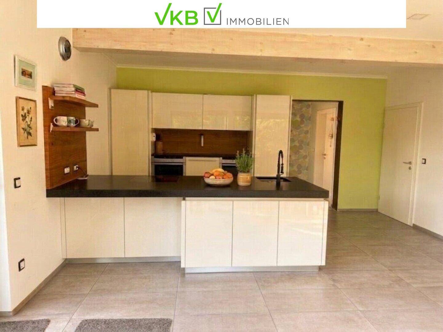 Moderne Küche mit weißen Hochglanzfronten, Kochinsel und grüner Akzentwand.