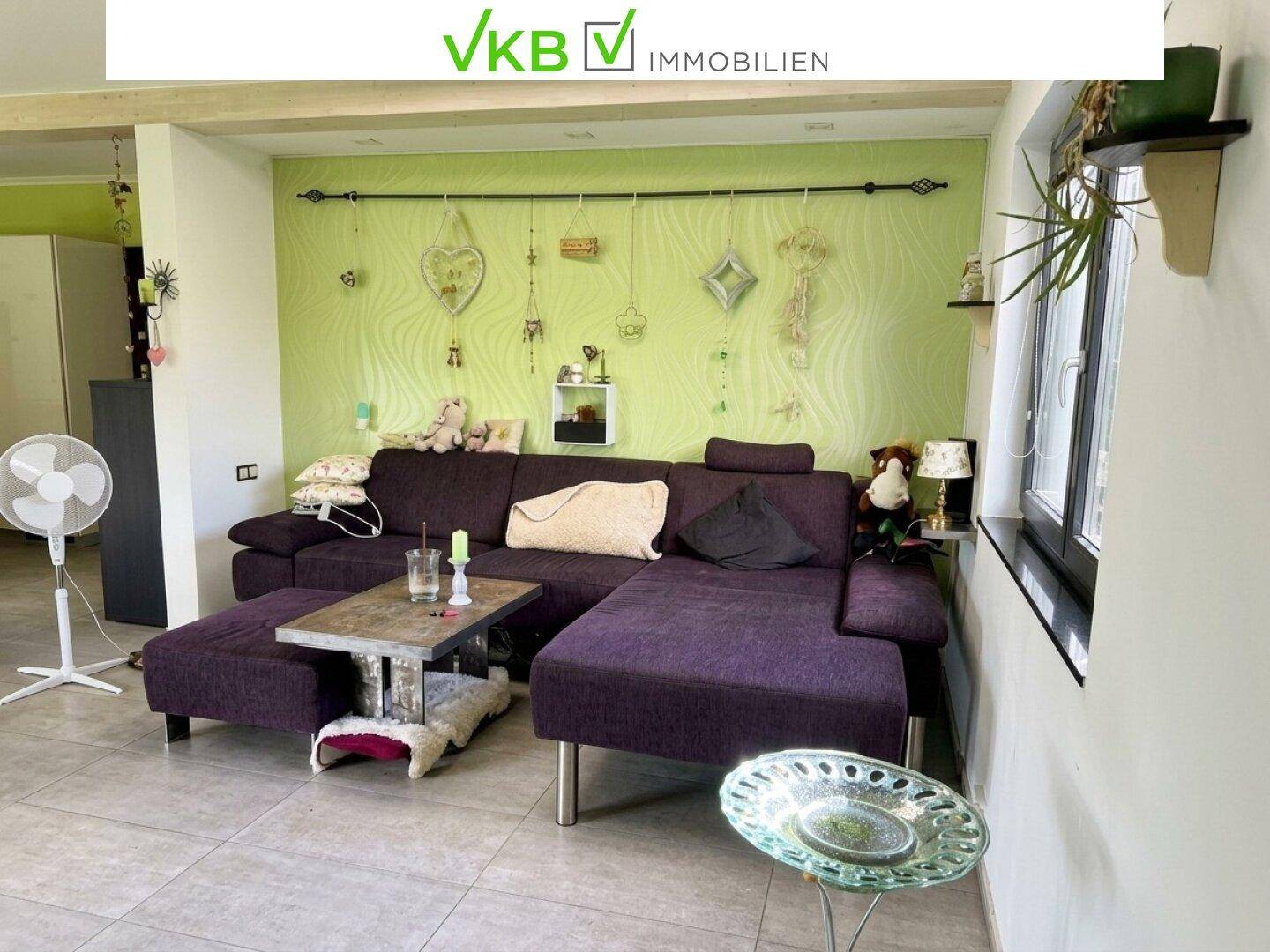 Gemütliches Wohnzimmer mit großer lila Couch, Fliesenboden und dekorierter grüner Wand.