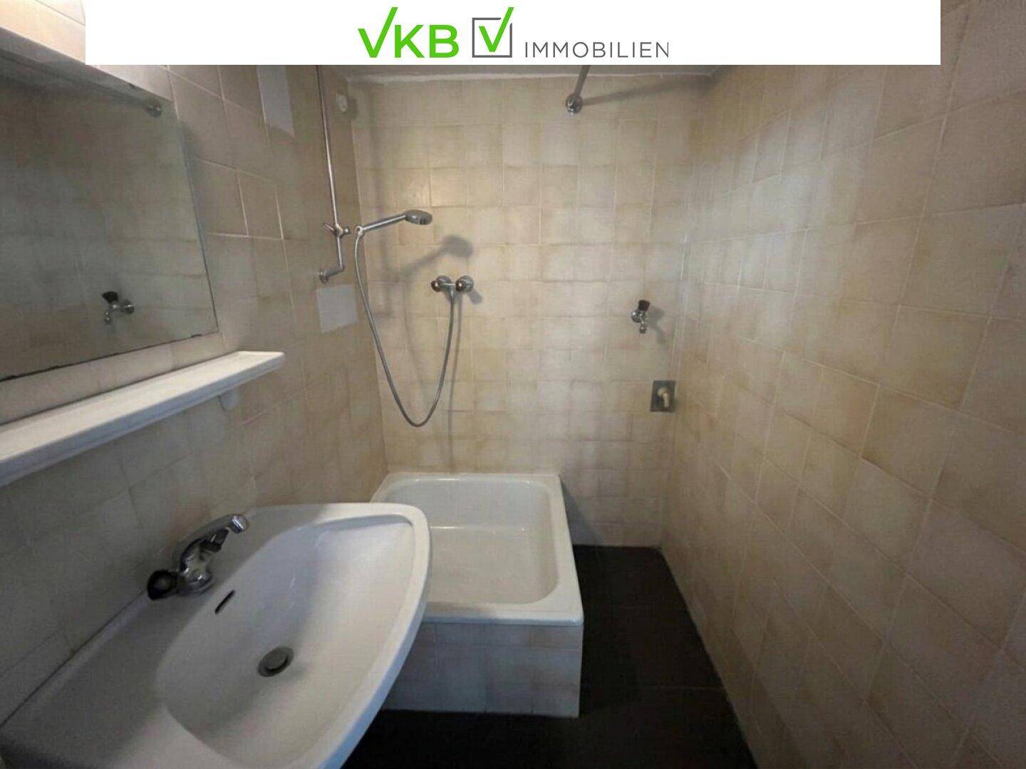 Badezimmer mit beigefarbenen Fliesen, Waschbecken und einer Badewanne mit Duschfunktion.