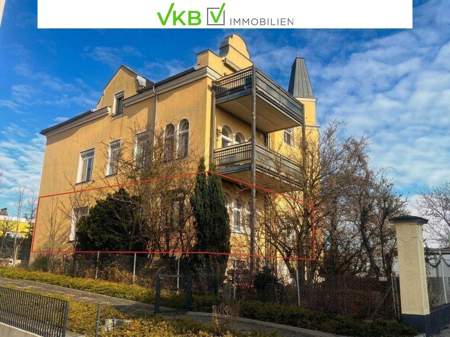 Historisches Gebäude mit gelber Fassade, Balkonen und einem markanten Turm, umgeben von kahlen Bäumen.