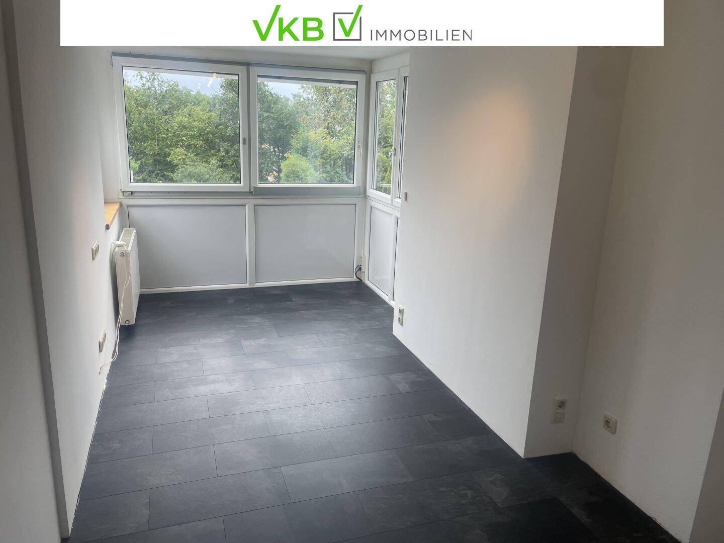 Geräumiges Zimmer mit dunklem Fliesenboden und großen Fenstern für viel Tageslicht.