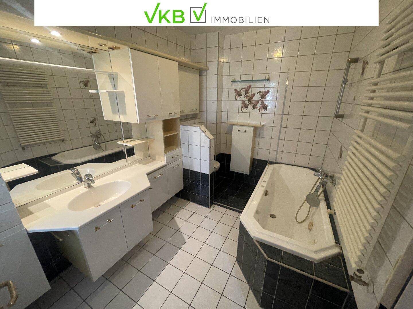 Geräumiges Badezimmer mit Eckbadewanne, Doppelwaschbecken und weißen sowie schwarzen Fliesen.