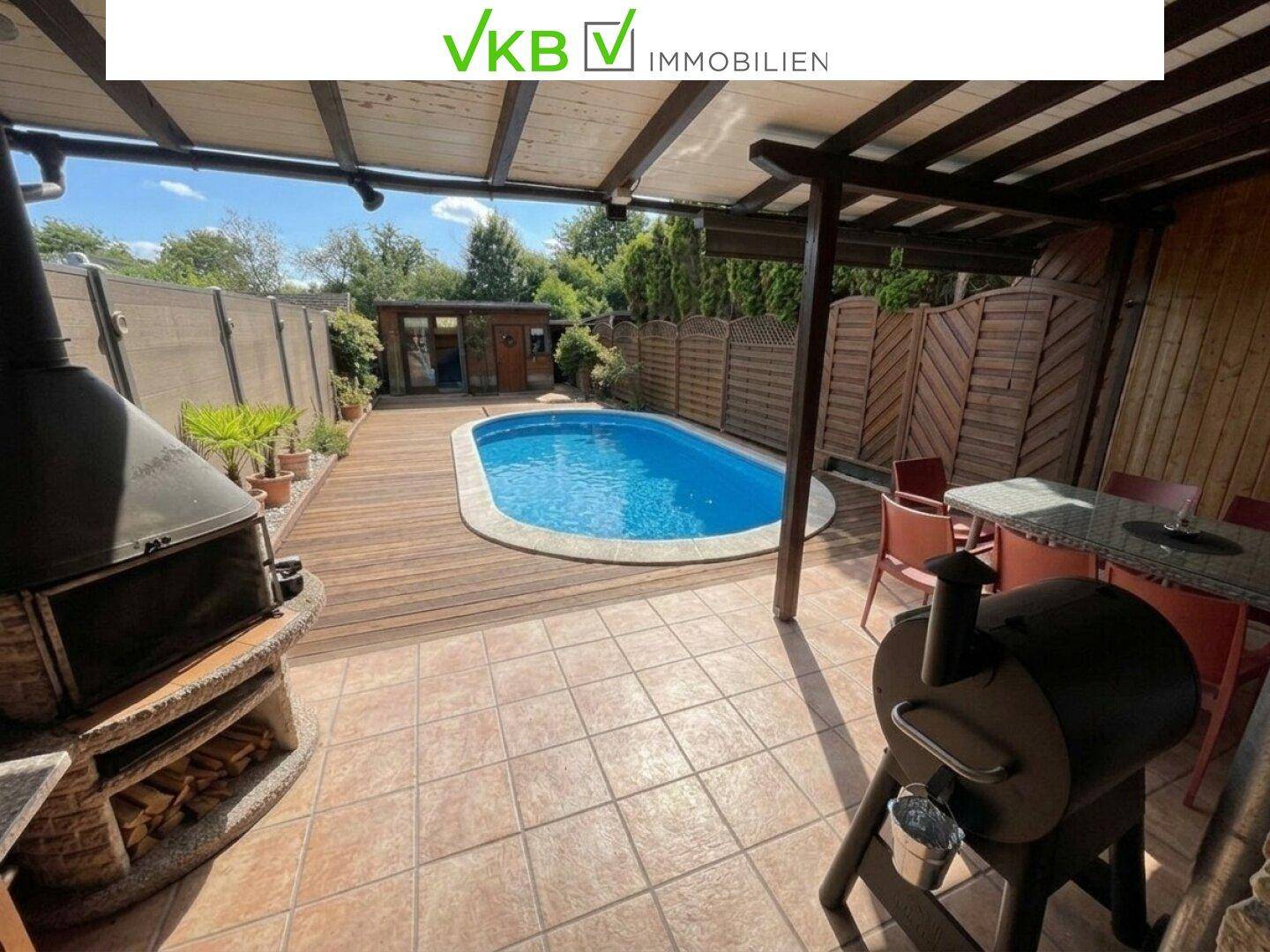 Geräumiger Gartenbereich mit Pool, gefliester Terrasse und Grillplatz unter einer Pergola.