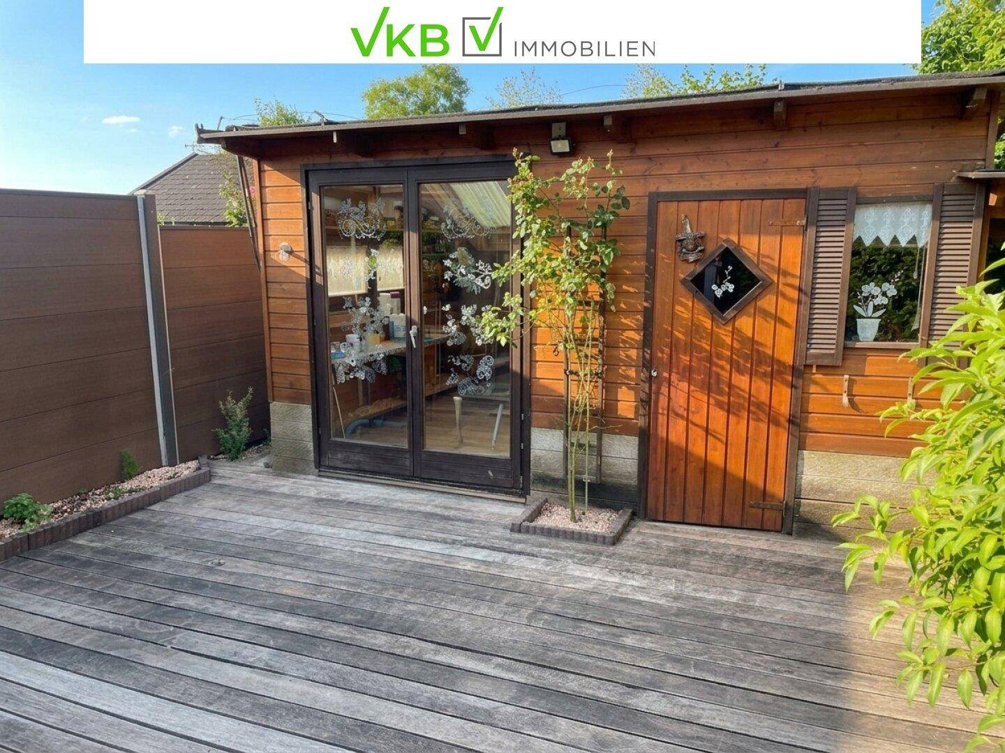 Charmantes Gartenhaus aus Holz mit großer Glasfront und angrenzender Holzterrasse.